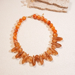 Detail of amber acrylic beads with marble texture and teardrop pendants on gold clasp