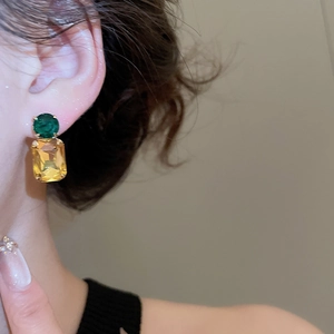Detail of geometric silver stud earrings with green round and yellow square gemstones