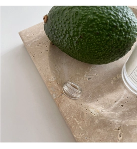 Minimalist silver multi-layered geometric ring on marble with candle and avocado