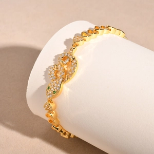 Detail of gold snake bracelet with zircon accents, green gemstone eyes and heart links