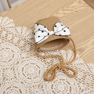Close-up of mini straw crossbody bag with white polka dot bow and metal zipper detail