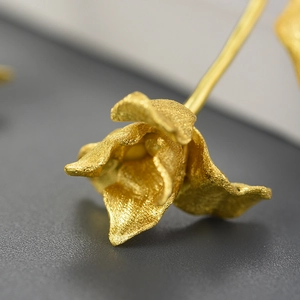 Macro shot showing the matte gold texture and intricate tulip petal detail of the earring