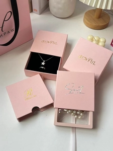 Detail of pink drawer-style jewelry boxes with gold foil logos on a white table