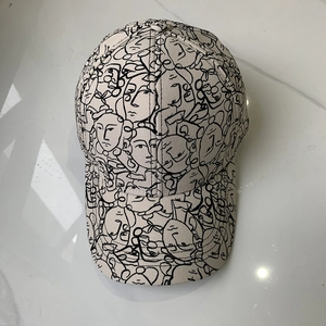 Off-white baseball cap with black abstract face line art print on marble background