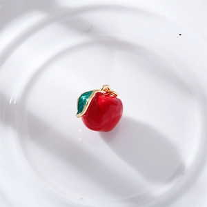 Detailed view of a red apple pendant with gold metal edges and green leaves for DIY jewelry