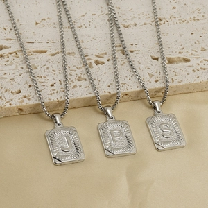 Three silver stainless steel square alphabet necklaces on a textured stone background