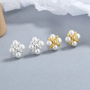 Detailed view of silver and gold pearl stud earrings with a four-petal flower design