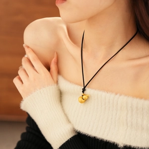 Detail view of a matte gold gourd pendant on a black woven cord necklace worn by a model