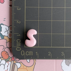 Detailed macro view of a pink resin S-letter accessory on a scaled cutting mat