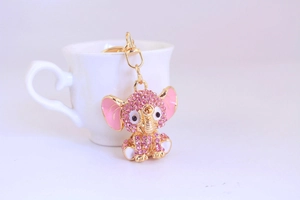 Detailed view of pink rhinestone elephant keychain with gold lobster clasp on white cup