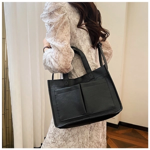 Detail view of the black PU leather tote bag showing large front pockets and long shoulder strap