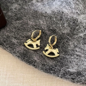 Close-up of 18k gold plated rocking horse earrings with hammered texture on fabric