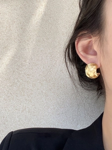 Close-up of golden woven texture C-shape earring worn by model in black suit