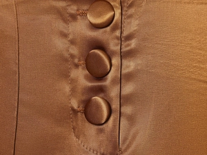 Detailed close-up of three satin-covered buttons on high-waist bronze trousers