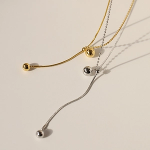 Detail of gold and silver snake chain necklaces with polished round bead pendants