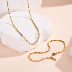 Detail of gold beaded necklace with lobster clasp and logo tag on stone display