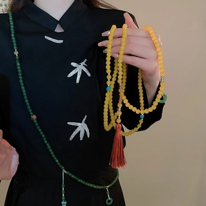 Détail du collier de 108 perles d'ambre avec pompon rouge sur chemise noire chinoise