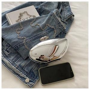 Silver reflective mango-shaped clutch bag with metal chain on a denim jacket backdrop