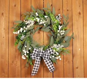 Detailed view of artificial green leaf wreath with white berries and black gingham bow