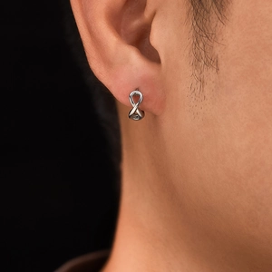 Close-up of a silver infinity symbol earring worn on the ear against a black background