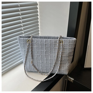 Close-up of light gray plaid tote bag with gold chain strap in natural sunlight