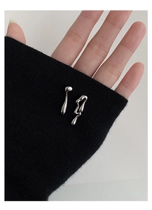 Macro shot of silver liquid metal earrings on a black knit sleeve detail