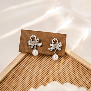 Elegant bow knot earrings with pearls and rhinestones on a wooden display stand