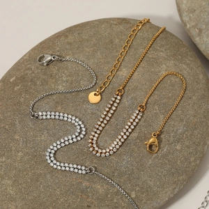 Minimalist gold and silver stainless steel zircon anklet set on a grey stone background