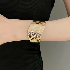 Close-up of a wide gold metal cuff bracelet with irregular lava texture on model wrist
