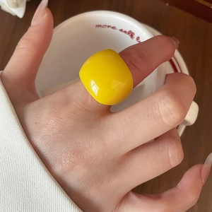 Close-up of a glossy yellow resin geometric ring worn on hand with an aesthetic background