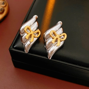 Close-up of gold and silver bow stud earrings displayed on a black leather jewelry box