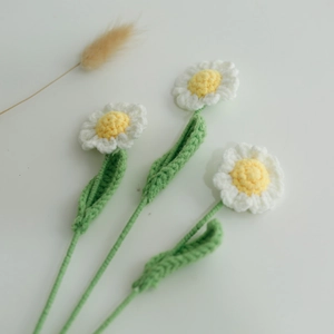 Close-up of three handcrafted white crochet daisies with yellow centers and green stems