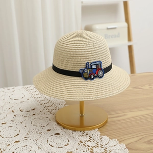 Détail d'un chapeau de paille enfant avec écusson de tracteur bleu et ruban noir