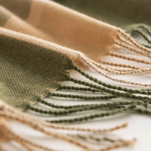 Close-up of green and beige plaid scarf with soft fringe and woven texture