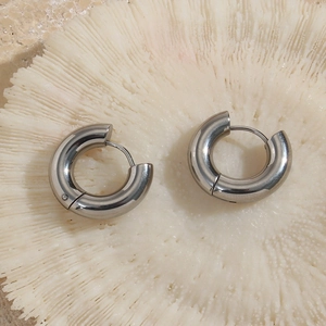 Detailed close-up of chunky silver titanium steel hoop earrings on white coral stone