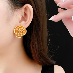 Close-up of elegant gold rose flower stud earrings worn by a model on dark background