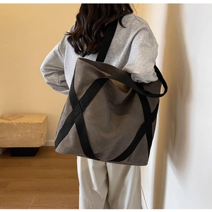 Detail of dark canvas tote bag featuring decorative black cross webbing and reinforced straps