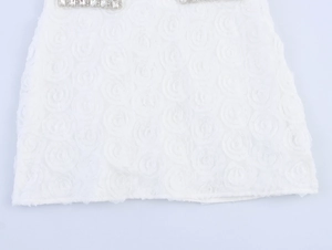 Détail de l'ourlet d'une robe blanche avec fleurs 3D et décorations en strass brillants