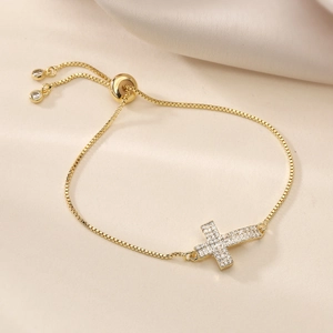 Gros plan d'un bracelet croix plaqué or 18 carats avec zircons sur fond de tissu beige