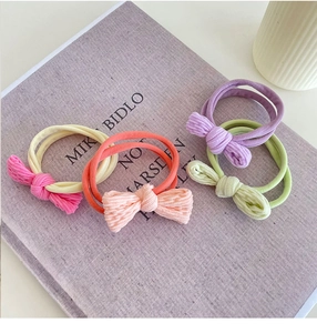 Elastic bow hair ties in pink, purple, and green on a minimalist book background