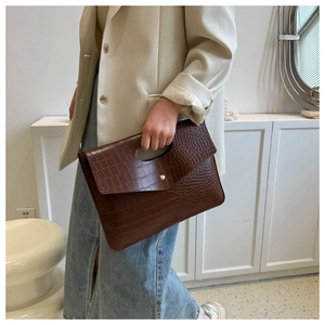 Detail of dark brown crocodile texture handbag with oval handle and gold metal clasp