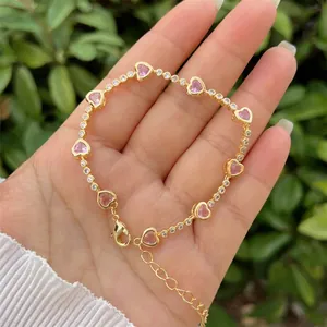 Dettaglio di gemme rosa a cuore e catena d'oro con fini zirconi sulla mano del modello
