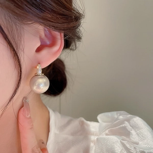 Détail de boucles d'oreilles créoles dorées avec zircons étincelants et une grosse perle blanche