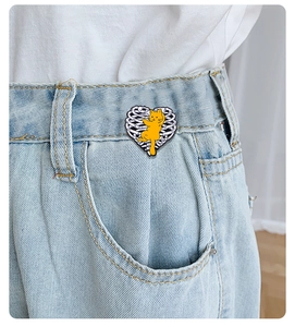 Detailed view of an orange cat enamel pin hugging a ribcage heart on blue denim fabric