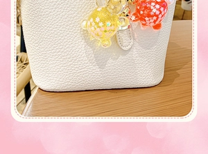 Detalle de bolso tipo cubo de cuero blanco con colgante de oso de resina naranja sobre madera