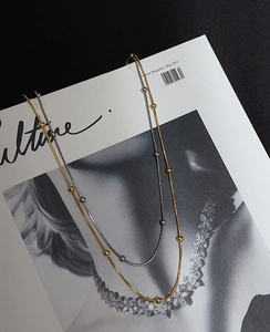 Flat lay of gold and silver snake bone necklaces with metal beads on a magazine background
