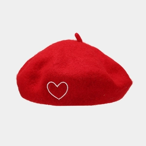 Close-up of red wool beret featuring white heart embroidery and top stem detail