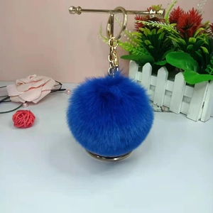 Portachiavi con pompon in finta pelliccia blu e anello dorato su sfondo floreale