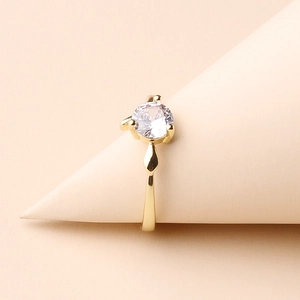 Detail of a minimalist gold-plated ring with a sparkling clear round gemstone on a cone