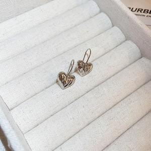 Macro detail of silver heart-shaped earrings with liquid metal texture on velvet box